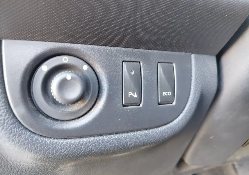 Gros plan sur les commandes de réglage des rétroviseurs et boutons ECO et assistance parking dans une Dacia Sandero Stepway beige dune 2020.