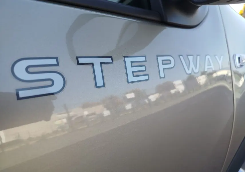 Gros plan sur l’inscription Stepway en lettres blanches sur la porte beige dune d’une Dacia Sandero Stepway 2020.