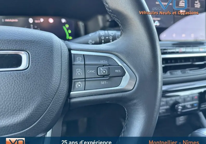 Gros plan sur les commandes du régulateur de vitesse au volant cuir du Jeep Compass blanc, tableau de bord en arrière-plan.