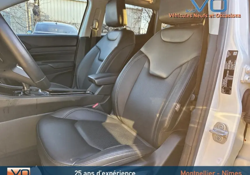 Vue intérieure côté conducteur du Jeep Compass blanc 2023, sièges cuir noirs avec accoudoir central visible.