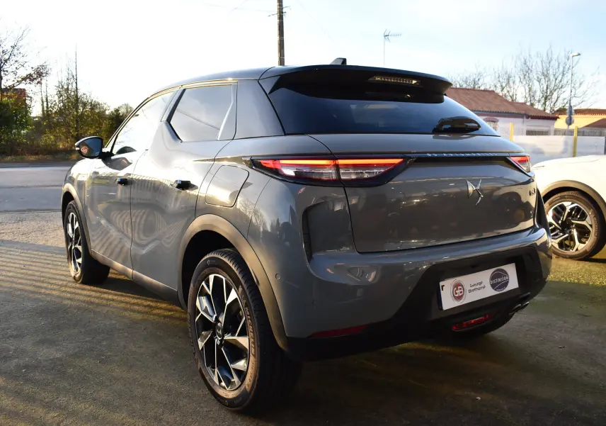 Vue 3/4 arrière droite d'un DS3 Crossback gris métallisé 2024 avec jantes noires et feux arrière LED allumés.