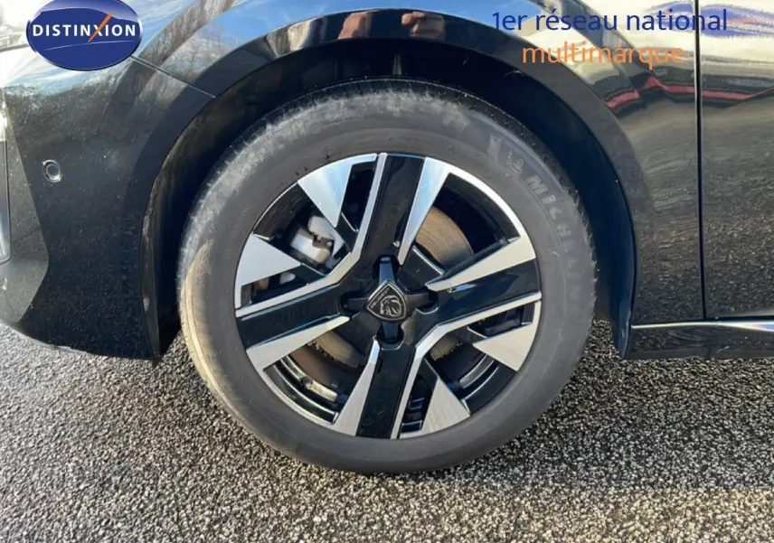 Gros plan sur la roue avant gauche noire d’une Peugeot 208 1.2 Hybrid 110ch avec jante alliage bicolore.