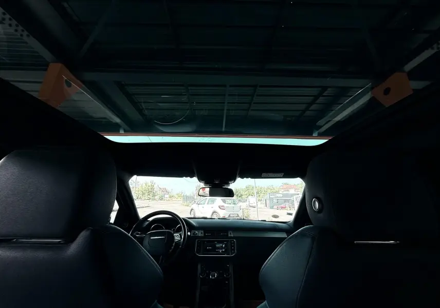 Vue intérieure du Range Rover Evoque noir 2017, montrant les sièges avant et le tableau de bord avec toit panoramique.