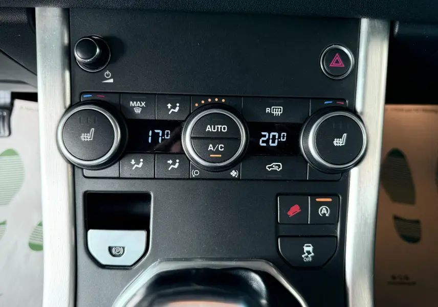 Gros plan sur la console centrale noire du Range Rover Evoque 2017, montrant les commandes de climatisation et d'assistance conduite.