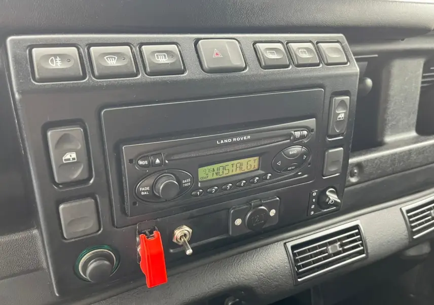 Tableau de bord noir du Land Rover Defender 90 Hard Top 2004 avec autoradio d'origine et interrupteurs alignés.