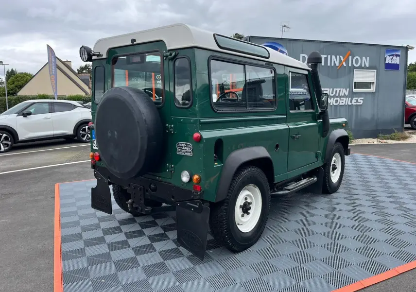 Vue 3/4 arrière droite du Land Rover Defender 90 vert avec Hard Top blanc, snorkel et marchepieds visibles.