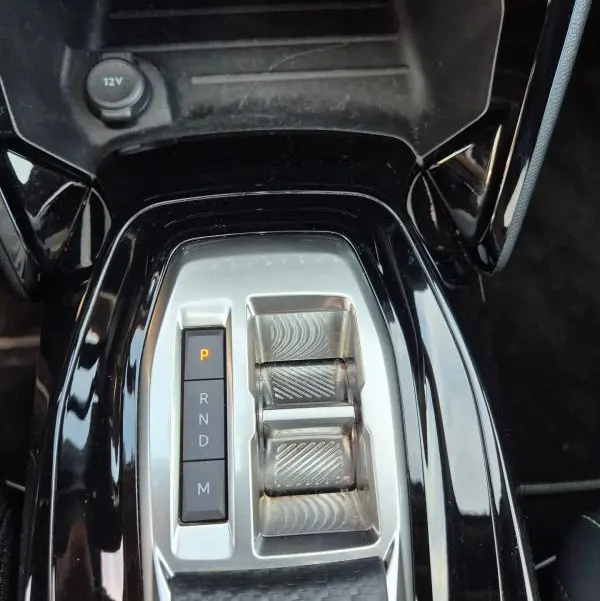 Vue rapprochée de la console centrale noire du Peugeot 2008 Hybrid 145 e-DCS6 GT avec sélecteur de boîte auto et prise 12V.