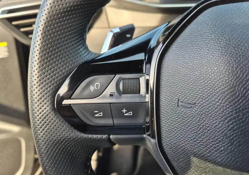 Gros plan sur les commandes gauche du volant noir perforé du Peugeot 2008 Hybrid 145 e-DCS6 GT 2024.