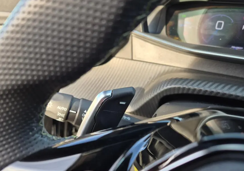 Gros plan sur la palette de changement de vitesse derrière le volant d’une Peugeot 2008 noir, intérieur carbone.