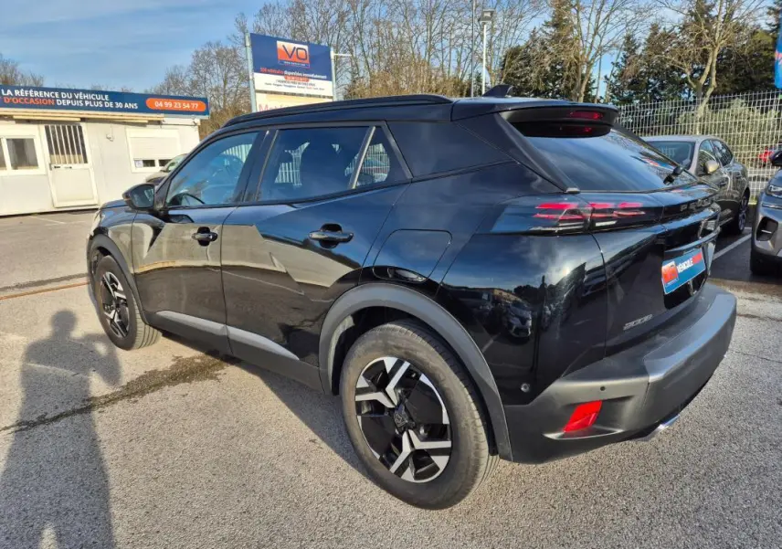 Vue 3/4 arrière droite d'un Peugeot 2008 Hybrid 145 noir avec jantes alliage 18 pouces et barres de toit visibles.