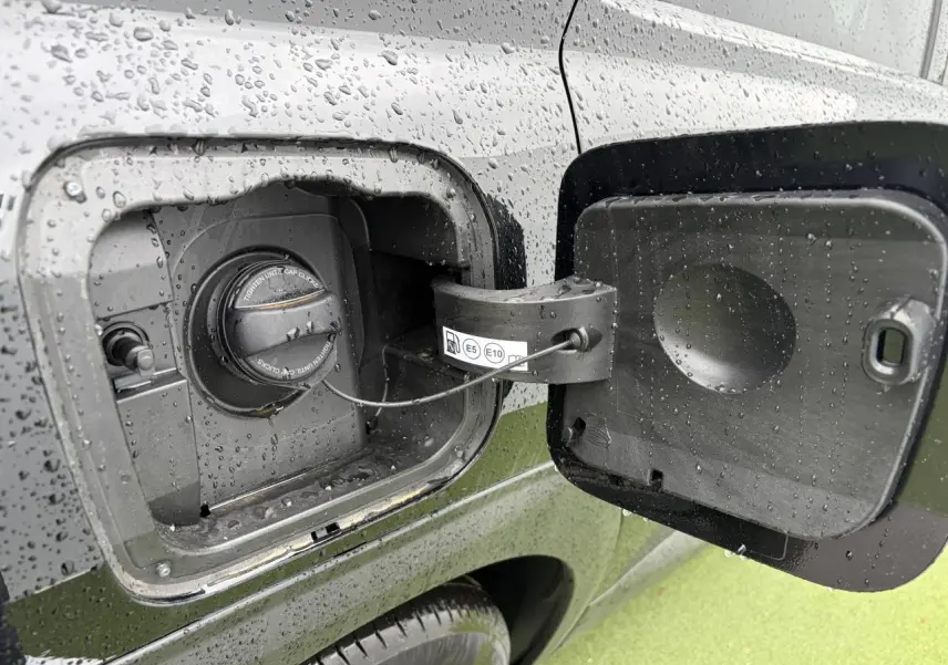 Gros plan sur la trappe de carburant ouverte du Citroën C5 Aircross noir métal, avec bouchon essence sous la pluie.