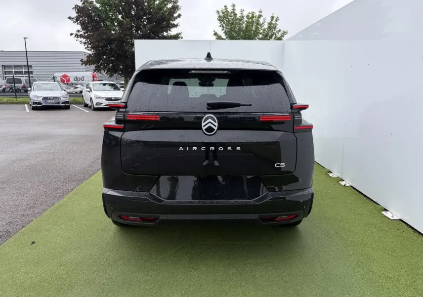Vue arrière d'un Citroën C5 Aircross noir métal avec feux arrière LED horizontaux et toit panoramique visible sous la pluie.
