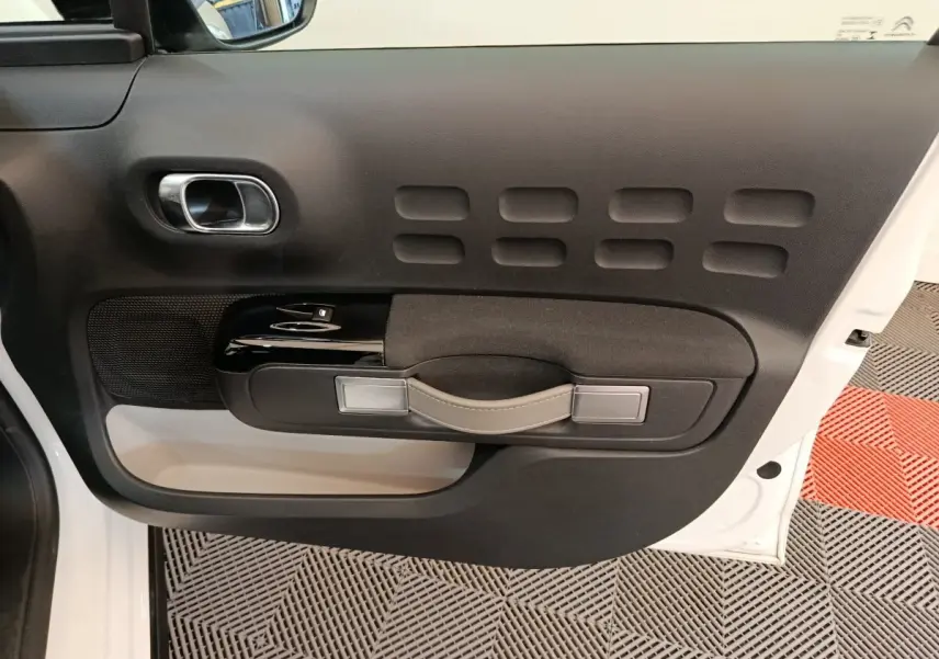 Vue intérieure du panneau de porte avant gauche blanc de la Citroën C3 avec poignée beige et commandes de vitres noires.