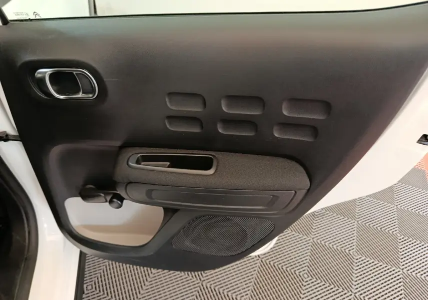 Vue rapprochée de la porte arrière droite noire de la Citroën C3 blanche, avec poignée et haut-parleur intégrés.
