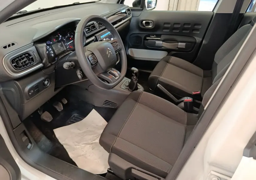 Intérieur de la Citroën C3 blanc, vue côté conducteur, montrant tableau de bord, volant multifonctions et sièges noirs.