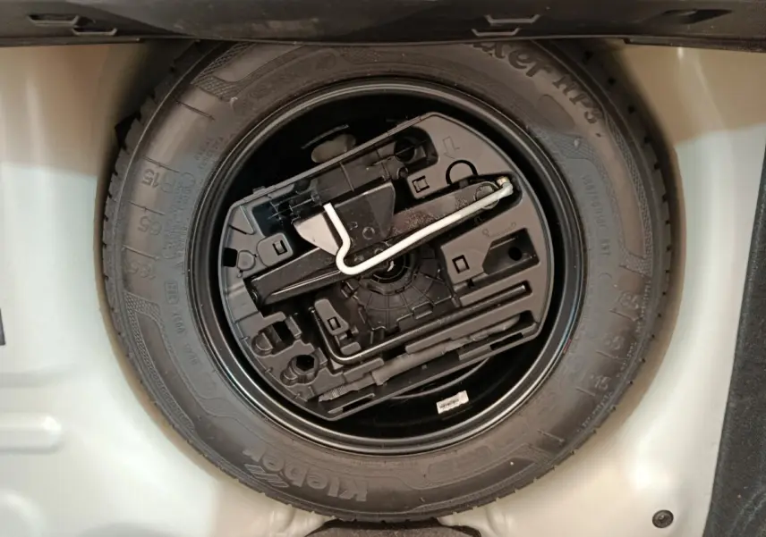 Gros plan sur la roue de secours noire avec kit de réparation intégré dans le coffre d'une Citroën C3 blanche.
