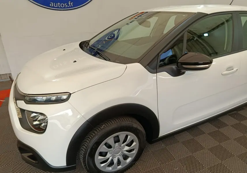 Vue 3/4 avant droit d'une Citroën C3 blanche avec rétroviseur noir et phares LED distinctifs.