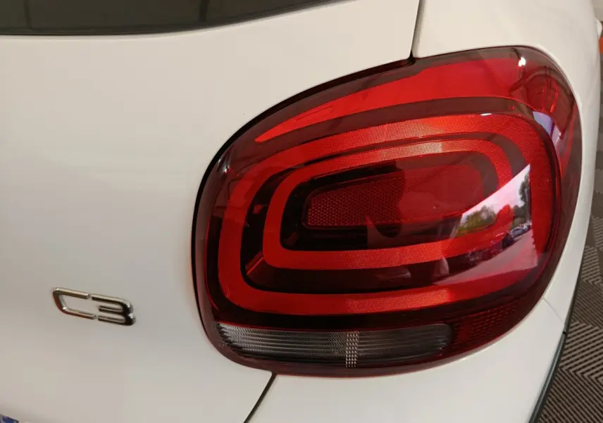 Gros plan sur le feu arrière droit rouge et le logo C3 d'une Citroën C3 blanche vue de l'arrière.