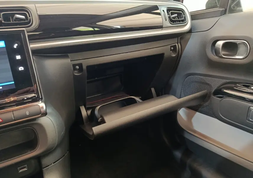 Vue intérieure côté passager du tableau de bord noir et gris avec boîte à gants ouverte d'une Citroën C3 blanche 2020.