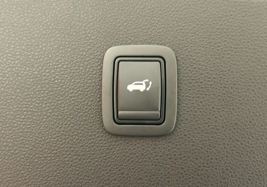 Bouton intérieur noir avec symbole blanc d'ouverture électrique du hayon sur fond de texture plastique grise.