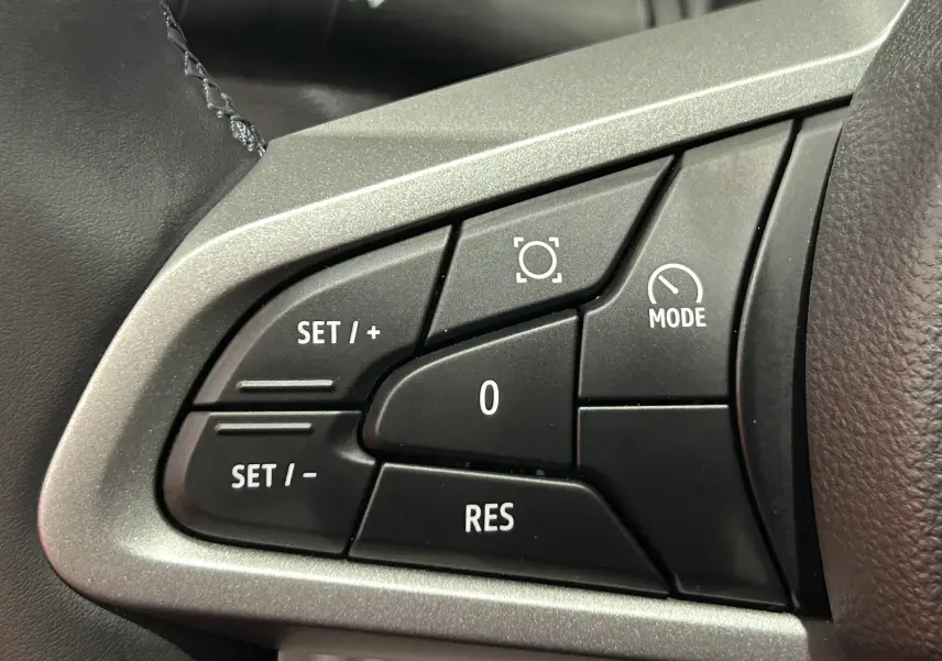 Détail des commandes au volant côté gauche du Dacia Bigster 2026, boutons noirs avec marquages blancs sur fond argenté.