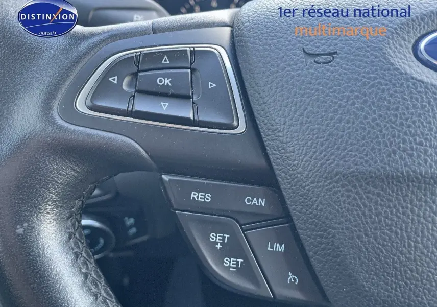 Gros plan sur le volant en cuir noir d'une Ford Focus SW gris magnetic, avec commandes multifonctions visibles.