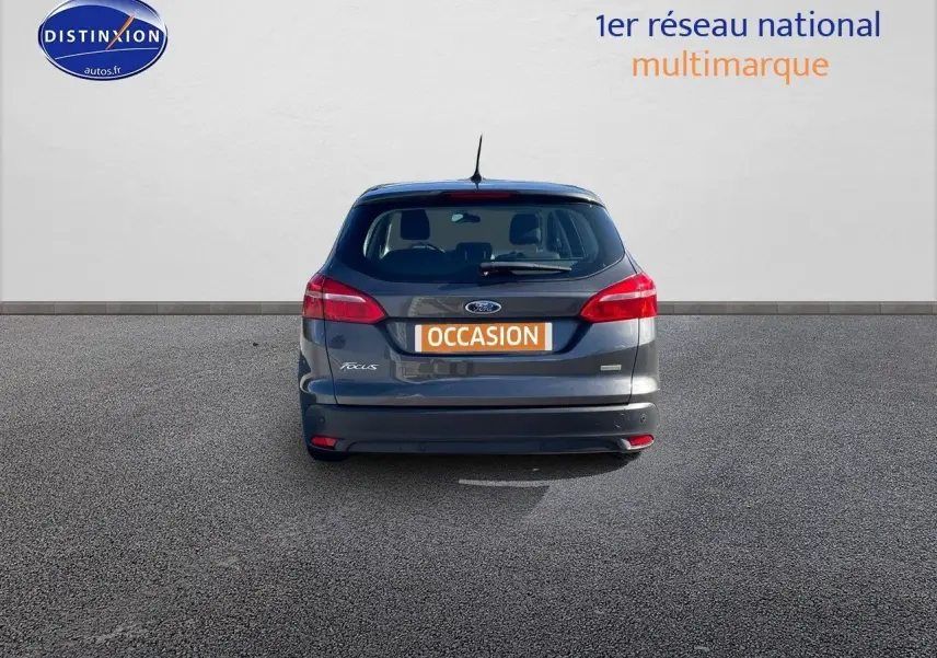 Vue arrière d'une Ford Focus SW gris magnetic metal avec plaque orange "OCCASION" sur un sol goudronné.