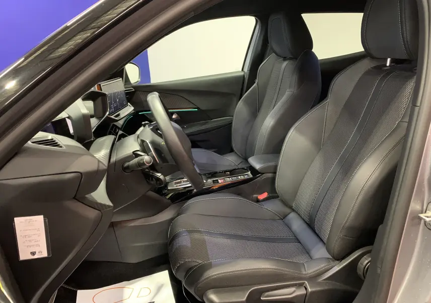 Intérieur avant droit du Peugeot 2008 gris 2023, sièges sport en cuir noir avec surpiqûres contrastées et tableau de bord moderne.