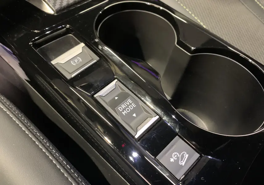 Gros plan sur la console centrale noire brillante du Peugeot 2008 gris 2023, avec boutons Drive Mode et frein à main électronique.