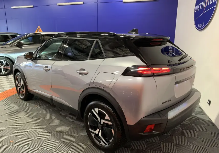 Peugeot 2008 BlueHDi 130 GT gris vue 3/4 arrière droit avec toit noir et feux arrière LED allumés.
