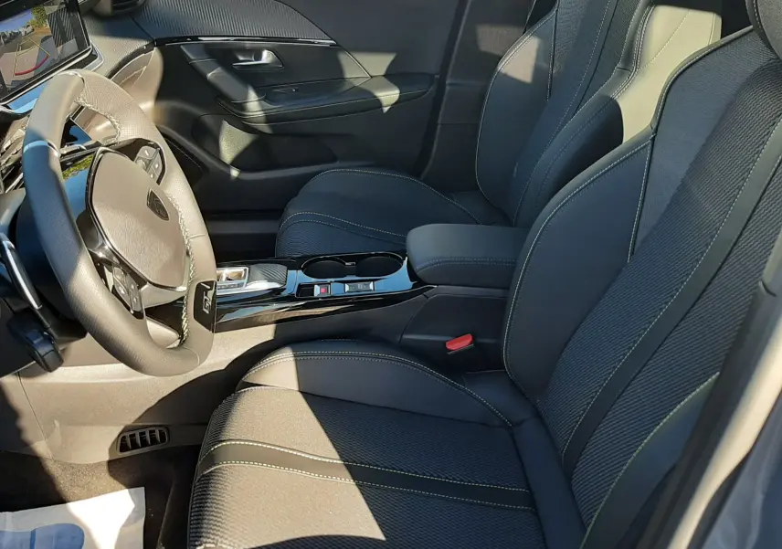 Intérieur du Peugeot 2008 2025 vu côté conducteur, sièges noirs avec surpiqûres vertes et console centrale brillante.