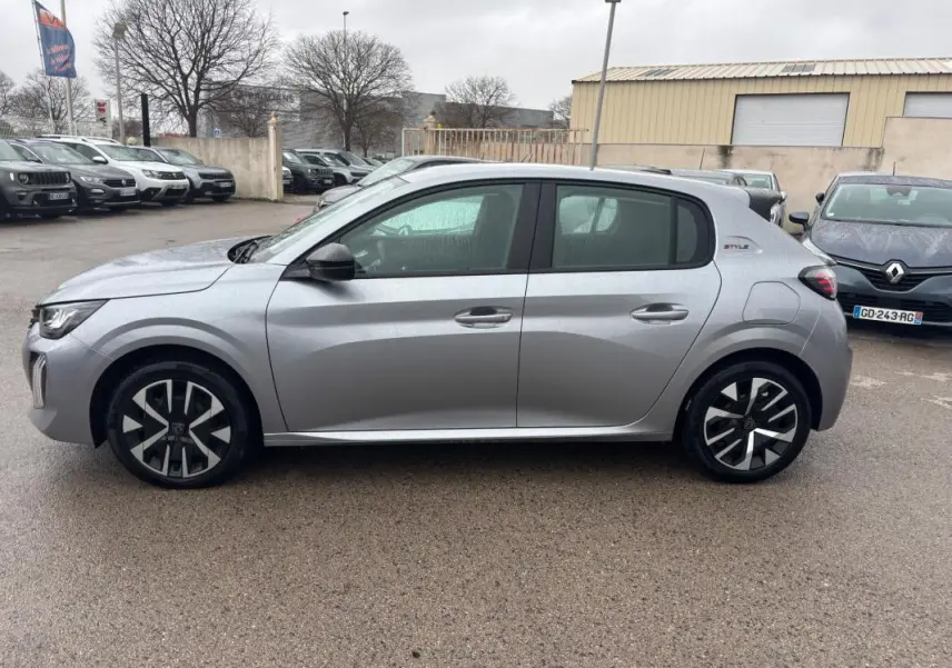 Vue de profil côté gauche d'une Peugeot 208 Hybrid 100 e-DCS6 Style gris avec jantes 16 pouces au parking.