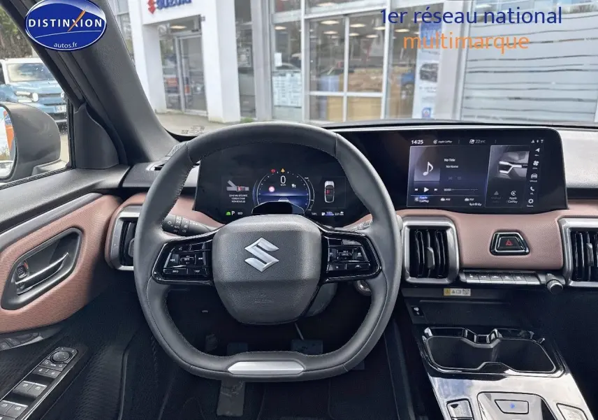 Vue intérieure avant centrée sur le volant Suzuki et tableau de bord avec écran tactile, garniture marron et noir.
