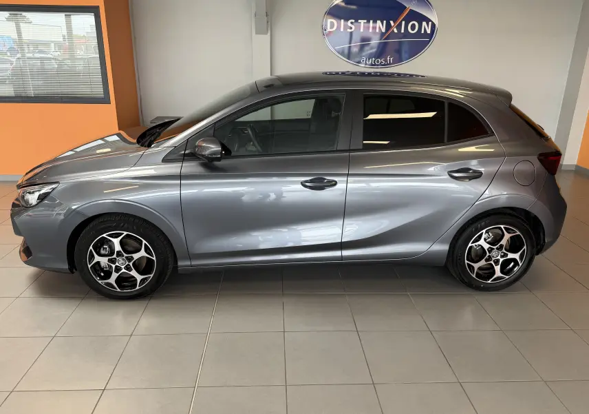 Vue de profil côté gauche d'une MG3 hybride gris métallisé avec jantes bi-ton et vitres surteintées en intérieur showroom.