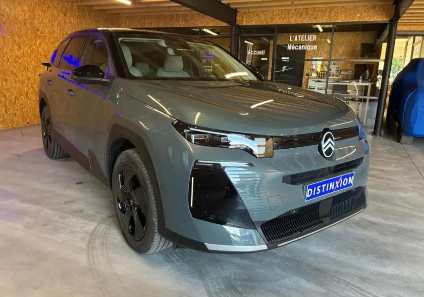 Vue 3/4 avant d'un Citroën C5 Aircross 2026 vert avec détails noirs et jantes noires, stationné en intérieur.