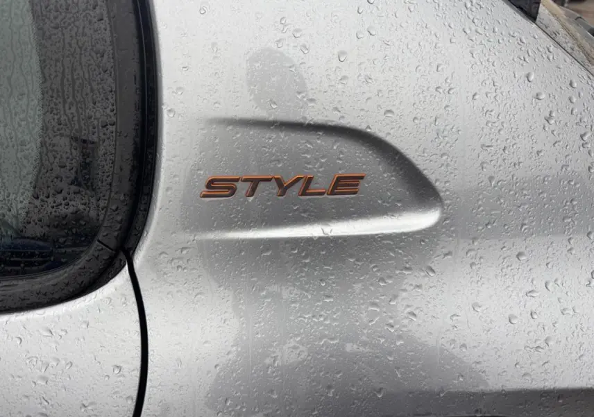Gros plan sur l'aile arrière droite grise d'une Peugeot 208 Hybrid 100 e-DCS6 Style avec logo "STYLE" sous la pluie.