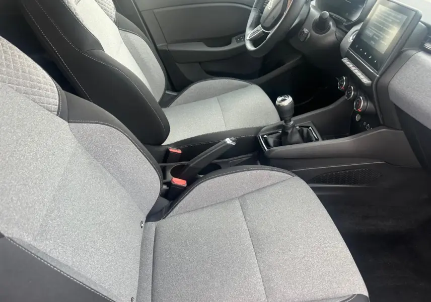 Vue intérieure côté conducteur de la Renault Clio V dCi 100 Evolution 2025, sièges gris et console centrale avec boîte manuelle.