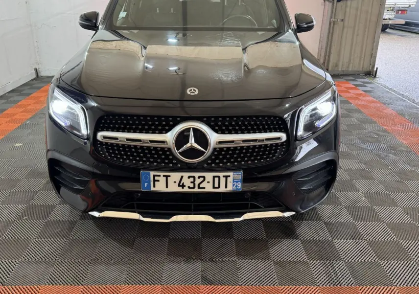 Vue de face du Mercedes GLB 200 d AMG Line noir avec calandre étoilée et phares LED allumés dans un garage.