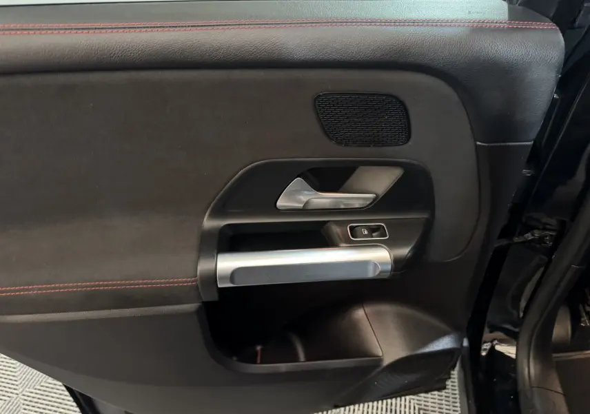 Gros plan sur la porte intérieure côté gauche noire du Mercedes GLB 200 d AMG Line avec surpiqûres rouges et poignée alu.