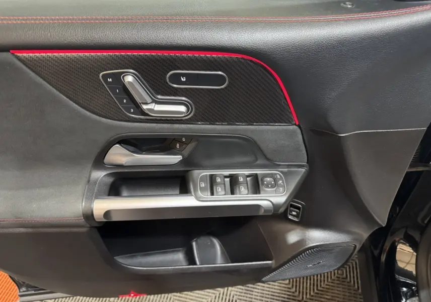 Gros plan sur la porte avant gauche noire du Mercedes GLB 200 d AMG Line avec commandes de sièges et bande rouge décorative.