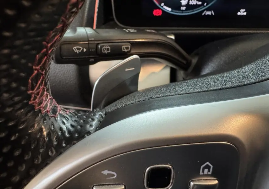 Gros plan sur le volant cuir noir avec surpiqûres rouges du Mercedes GLB 200 d AMG Line, affichage digital en arrière-plan.