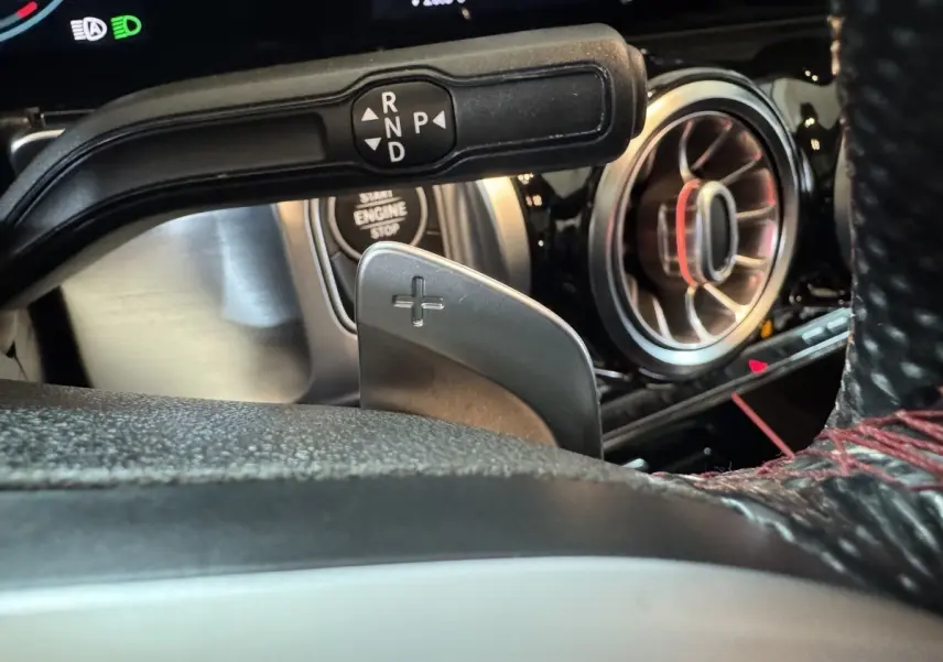 Gros plan sur la commande de boîte automatique et la sortie d'air ronde chromée du tableau de bord d'un Mercedes GLB 200 d noir.