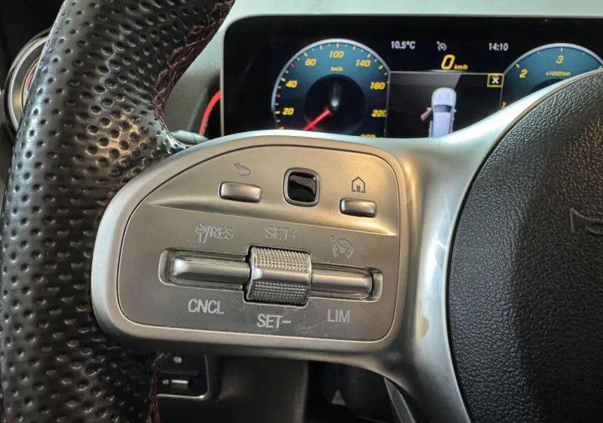 Gros plan sur les commandes du volant cuir perforé du Mercedes GLB 200 d AMG Line noir, avec tableau de bord numérique en arrière-plan.