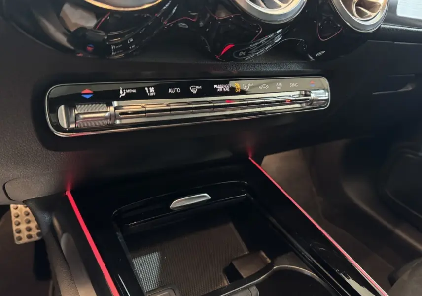 Vue rapprochée de la console centrale noire du Mercedes GLB 200 d AMG Line avec commandes climatisation et éclairage d’ambiance rouge.