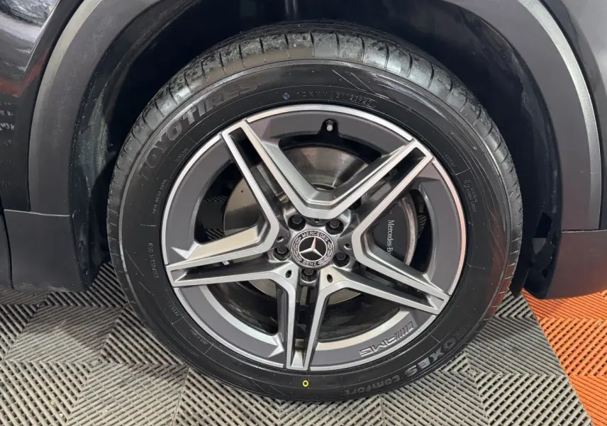 Gros plan sur la roue avant droite noire du Mercedes GLB 200 d AMG Line avec jante AMG à cinq branches.