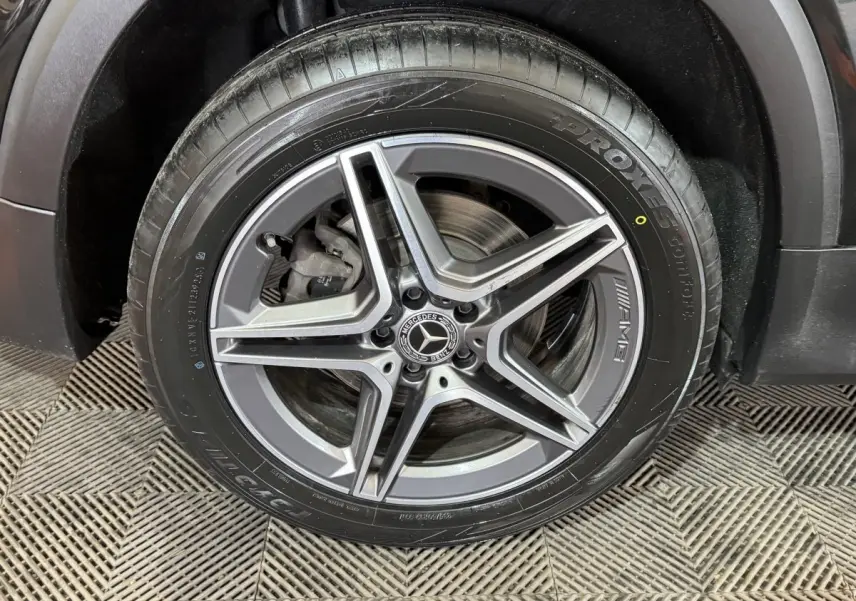 Gros plan sur la roue avant gauche noire du Mercedes GLB 200 d AMG Line avec jante AMG à cinq branches.