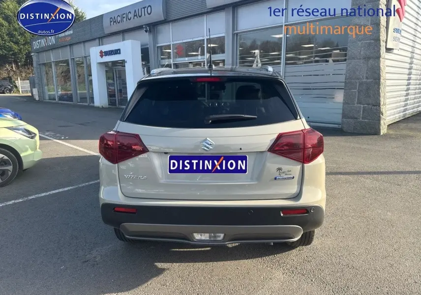 Vue arrière du Suzuki Vitara 1.4 Boosterjet Hybrid 2026 en beige So'Color Savanna Ivory avec toit noir et feux rouges.