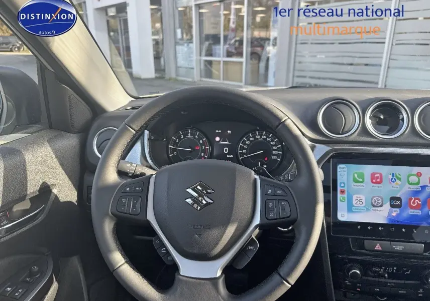 Vue intérieure centrée sur le volant cuir multifonction du Suzuki Vitara 1.4 Boosterjet Hybrid avec écran tactile et tableau de bord.