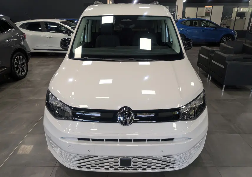Vue avant d'un Volkswagen Caddy blanc 2025 en showroom, avec calandre noire et logo VW centré.