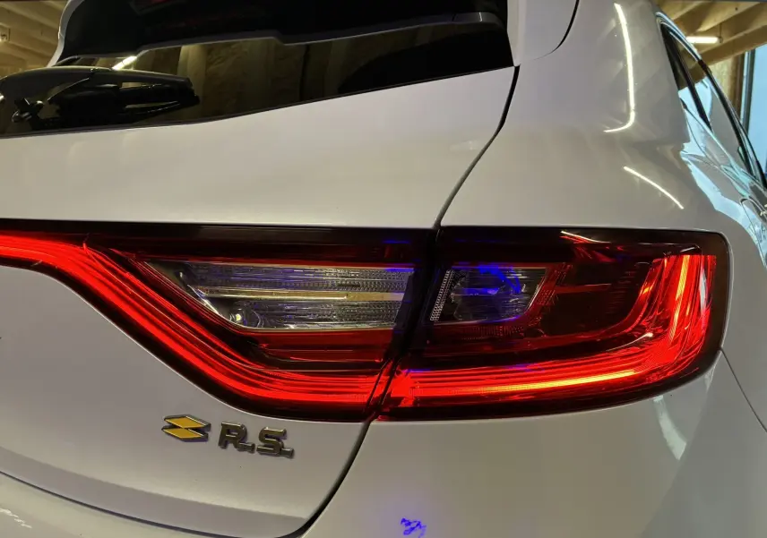 Gros plan sur le feu arrière droit rouge et blanc d'une Renault Mégane IV RS 280 blanche avec logo R.S. visible.